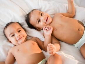 Identifica cuál es la diferencia entre los gemelos y los mellizos. Bebés gemelos sonriendo acostados en la cama.