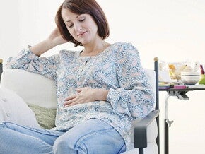 Mujer embarazada de un mes, sentada en un sofá, acariciando su vientre y sonriendo.