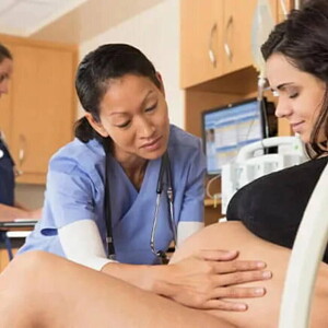 Mujer en trabajo de parto acostada en la camilla de hospital, sonriendo y con una doctora acariciando su vientre.