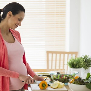 Mujer embarazada en la cocina cortando verduras para una alimentación saludable