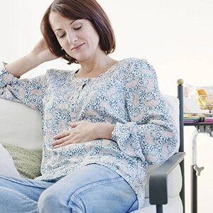 Mujer embarazada de un mes, sentada en un sofá, acariciando su vientre y sonriendo.