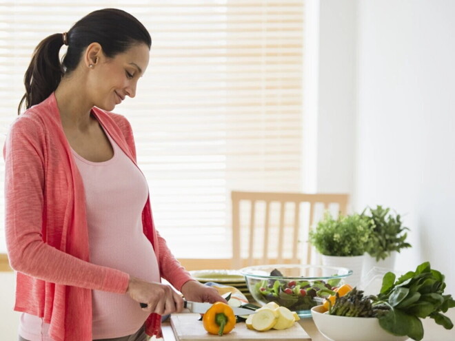 Alimentación saludable en el embarazo Mujer embarazada en la cocina cortando verduras para una alimentación saludable