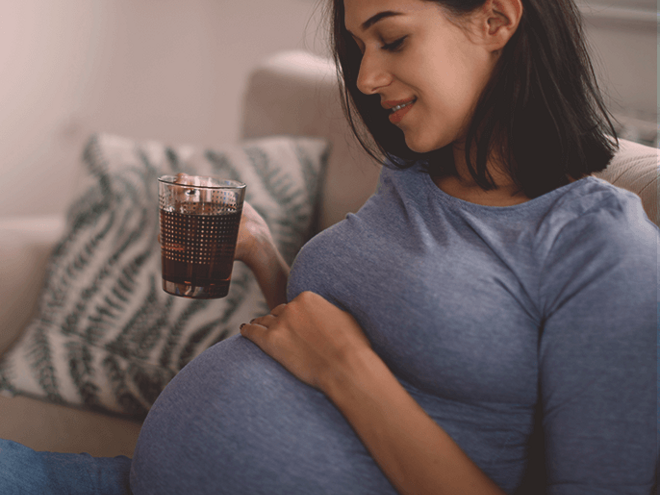 Pregnant woman on a couch, drinking tea and smiling.