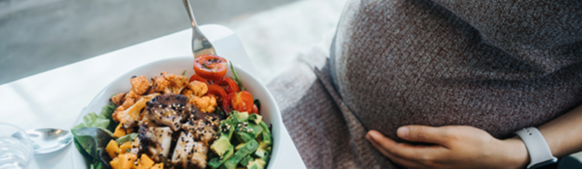 Mujer embarazada en la cocina comiendo ensalada con verduras variadas. Nutrición en el embarazo.