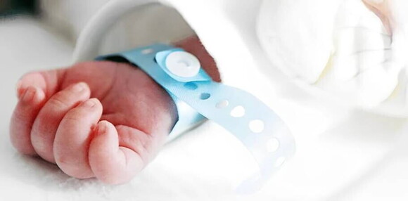 Mano de bebé varón recién nacido con pulsera azul de hospital.