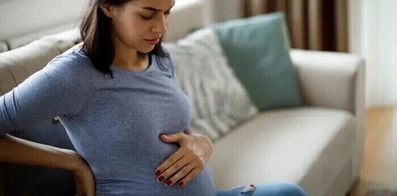 Mujer embarazada sentada en un sofá tocando su vientre, visiblemente sintiendo molestias