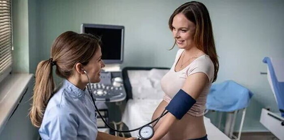 Mujer embarazada sentada en la camilla del hospital sonriendo mientras la doctora le mide la presión.