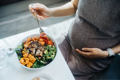 Mujer embarazada en la cocina comiendo ensalada con verduras variadas. Nutrición en el embarazo.